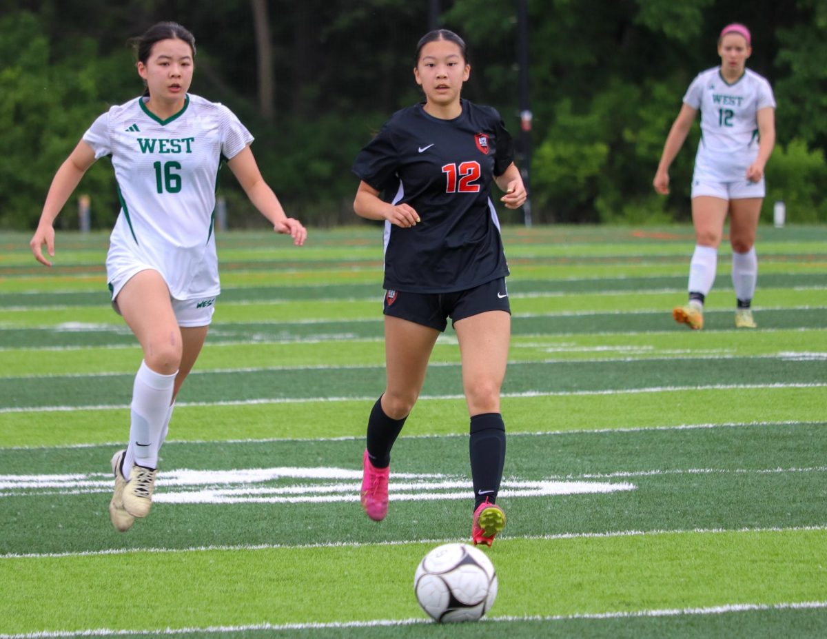 Simay Zhu (12) pushes the ball upfield while being defended by Ellie Chen (16) of Iowa City West