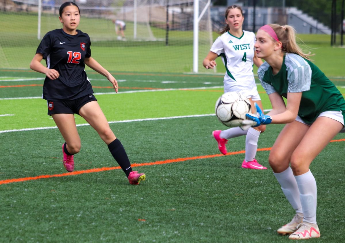 Little Cyclone Simay Zhu (12) applies defensive pressure to Trojan goalie Lila Eastvold.