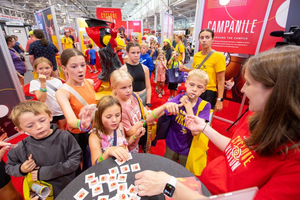 A group of about 15 children gather around a table at the Iowa State Fair exhibit to get waterless temporary Cyclone tattoos from an Iowa State staff member.